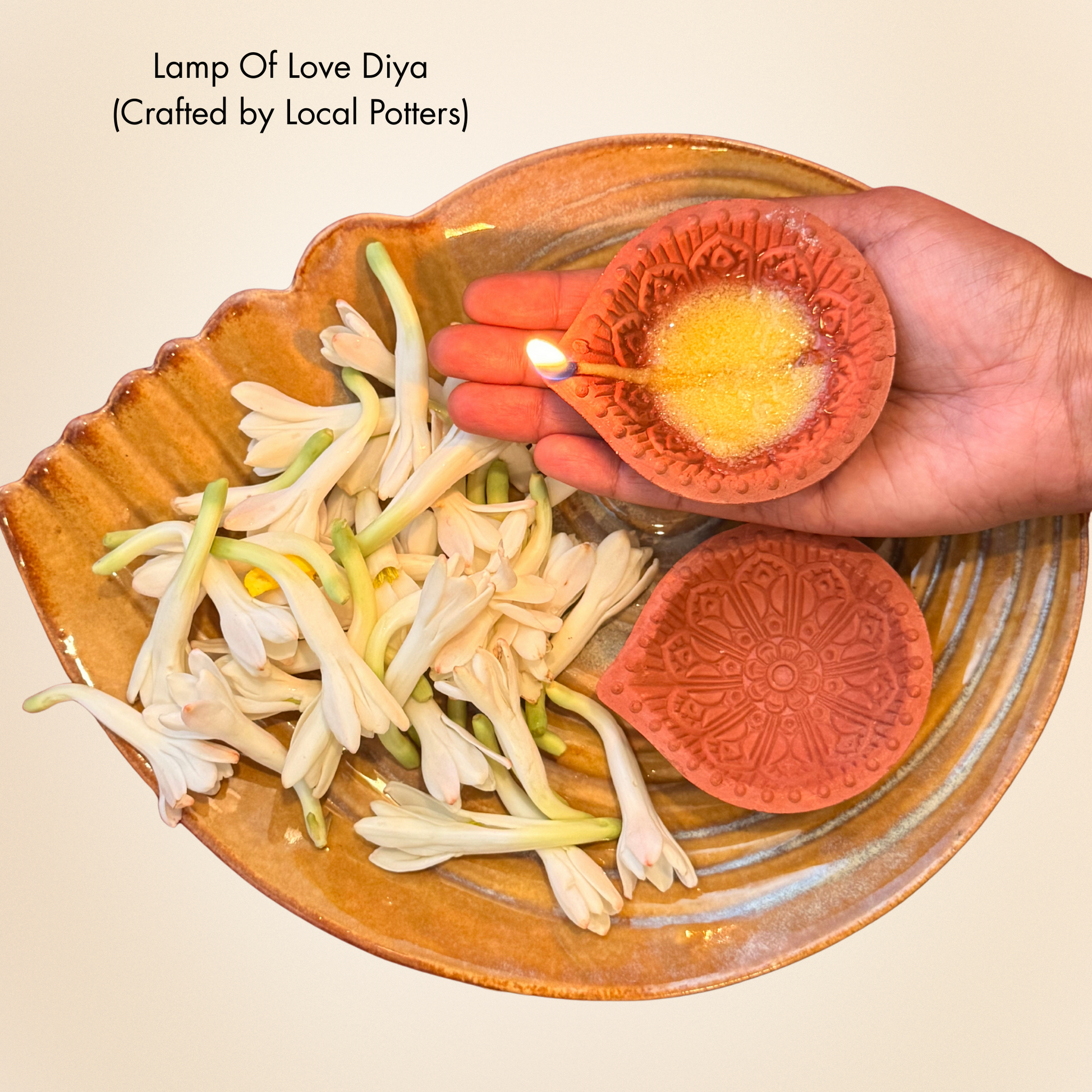 Ceramic diya being lit with a hand, surrounded by flowers on a wooden plate.
