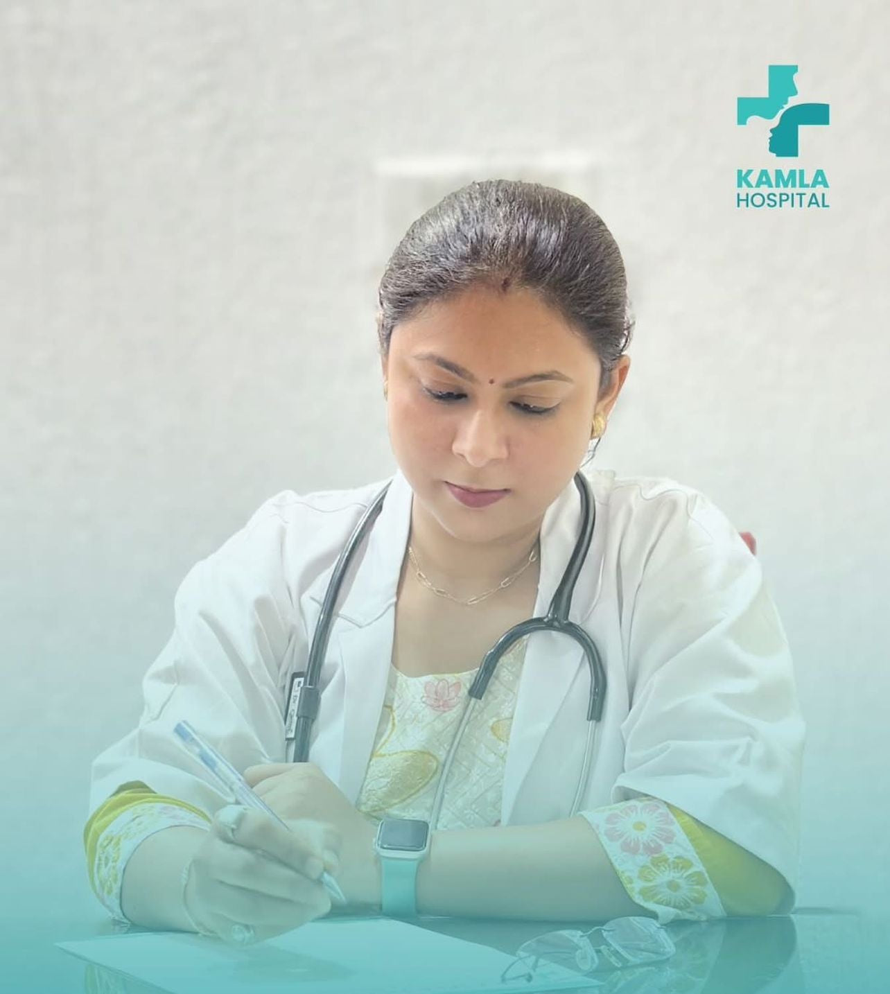Doctor in a white coat with a stethoscope, sitting at a desk with Kamla Hospital logo in the corner.