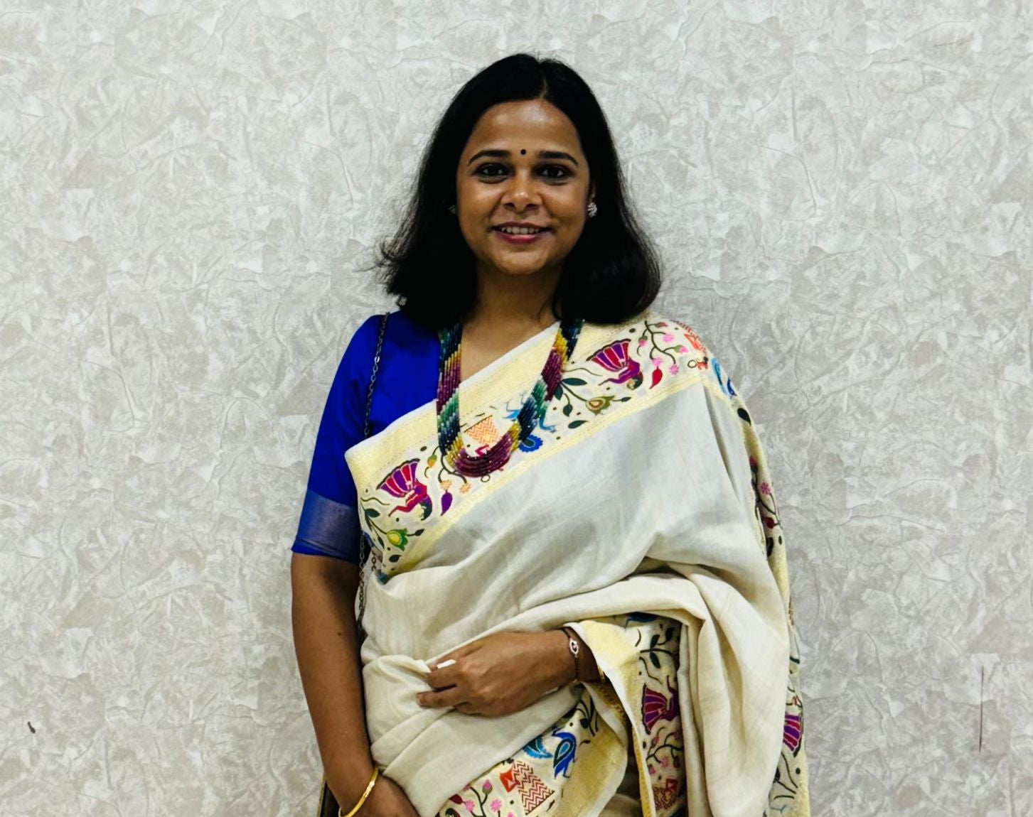 Woman wearing a white saree with floral patterns against a light gray background